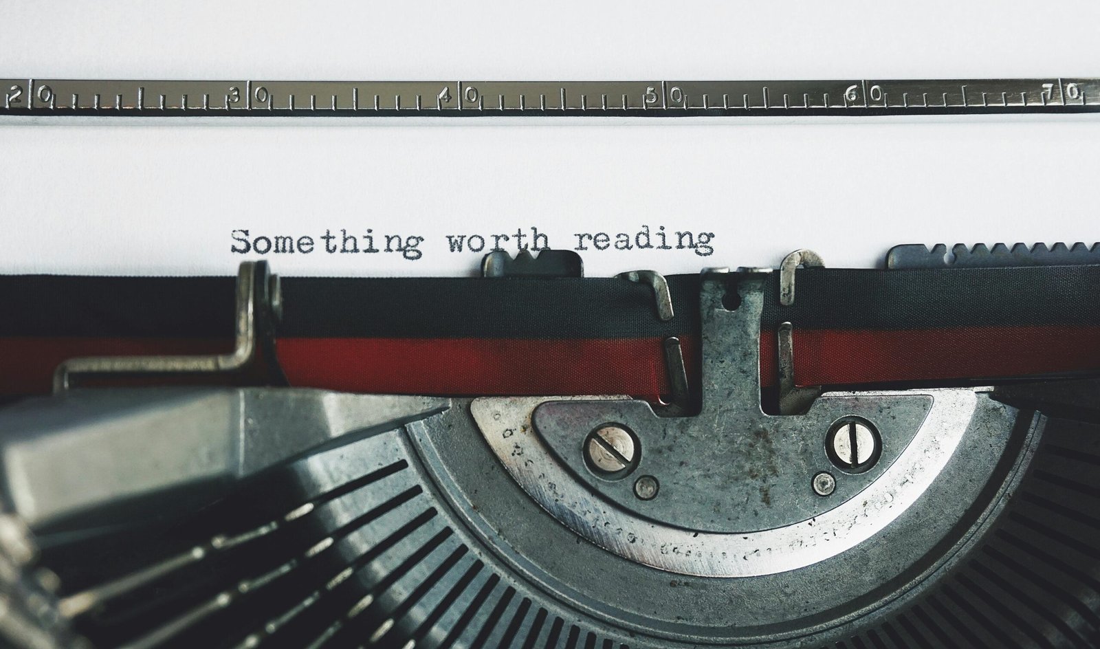 A close-up of a vintage typewriter typing the words “Something worth reading” on white paper.